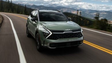 A green 2023 Kia Sportage driving down a highway.