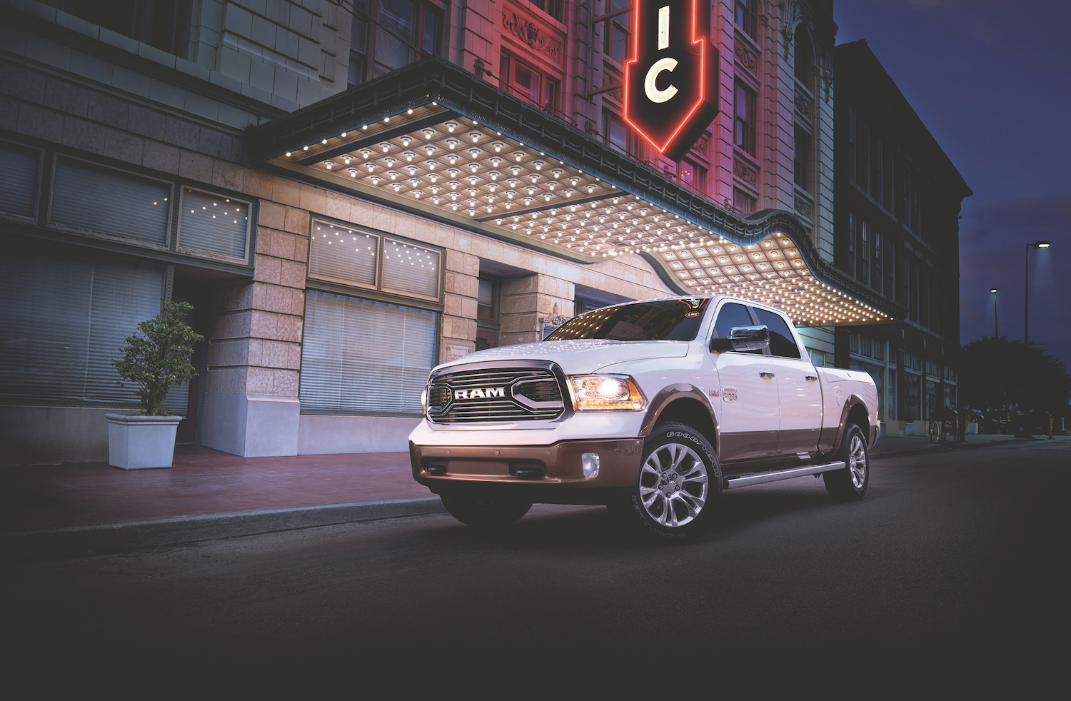 A white Ram truck parked in front of a building in the city with neon lights.
