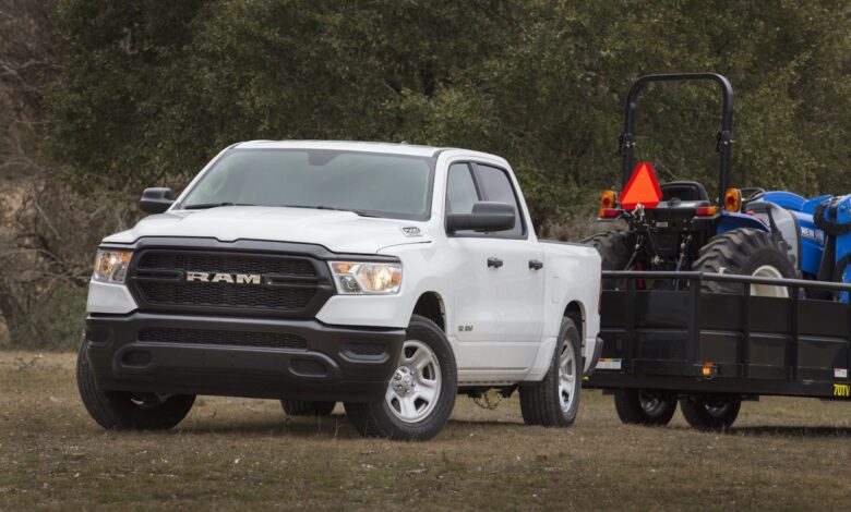 A white Ram 1500 tradesman work truck hooked up to a trailer with a tractor on top of it.