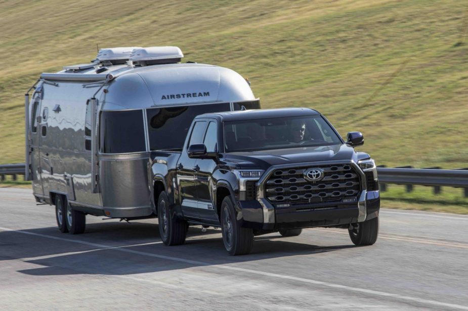 Advertising image of a 2023 Toyota Tundra pulling an Airstream travel trailer on a highway, a green hillside visible in the background.