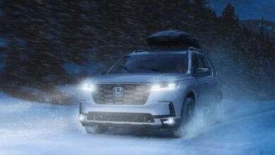 A white 2023 Honda Pilot midsize SUV is driving in the snow.