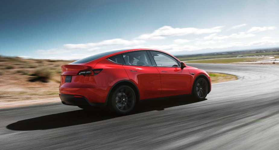 A small red Tesla Model Y electric SUV is driving on the road. 