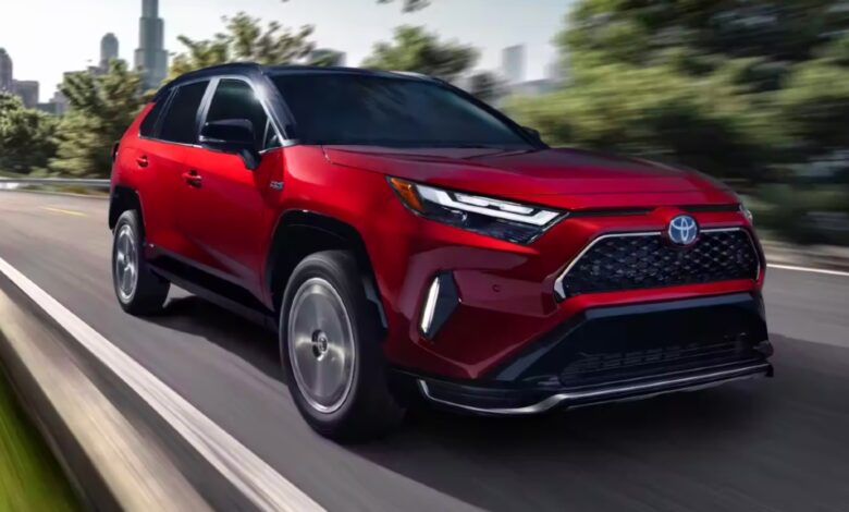 A red 2023 Toyota RAV4 Prime small plug-in hybrid SUV is driving on the road.