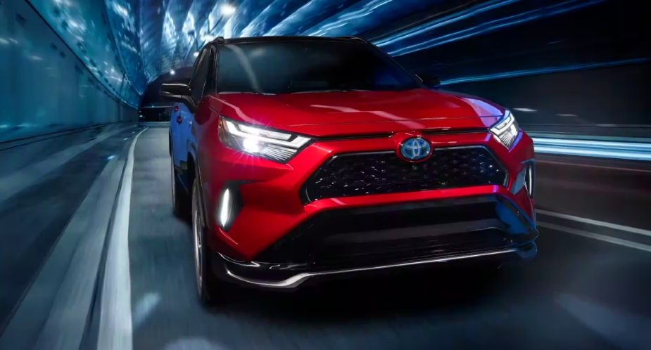 A small red 2023 Toyota RAV4 Prime plug-in hybrid SUV is driving on the road. 