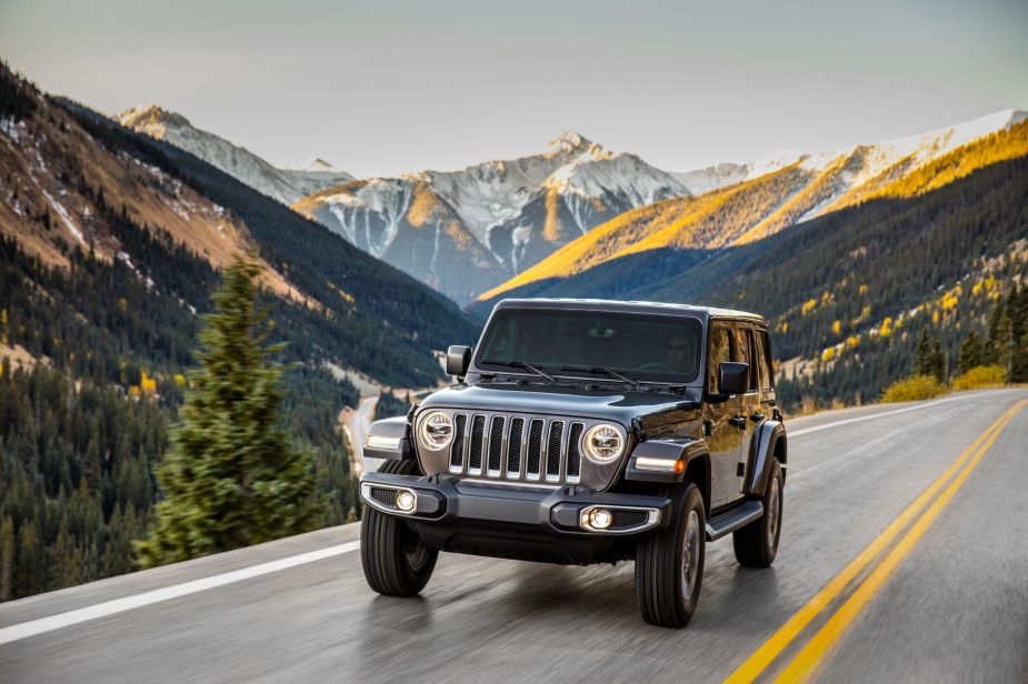 A dark gray Jeep Wrangler Unlimited off-road SUV model driving on a highway near the mountains
