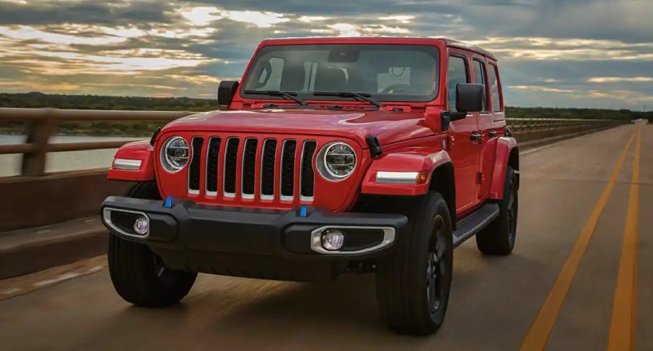 A small red 2023 Jeep Wrangler SUV is driving on the road. 