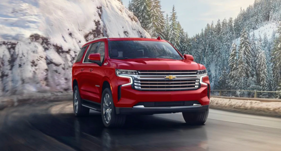 A red 2023 Chevrolet Suburban full size SUV is driving on the road.