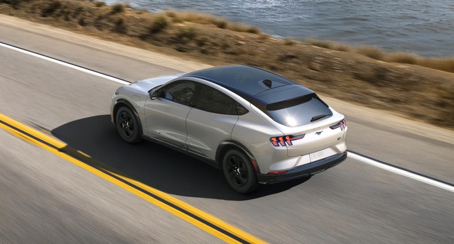 A small white 2023 Ford Mustang Mach-E electric SUV is driving on the road. 