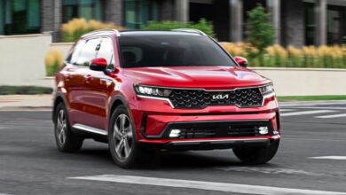 A red Kia Sorento Hybrid midsize hybrid SUV is driving on the road.