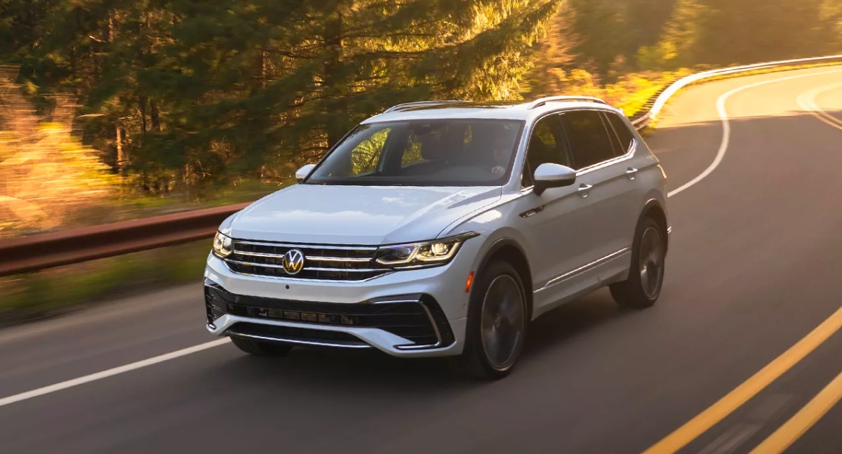 A small white 2023 Volkswagen Tiguan SUV is driving on the road.