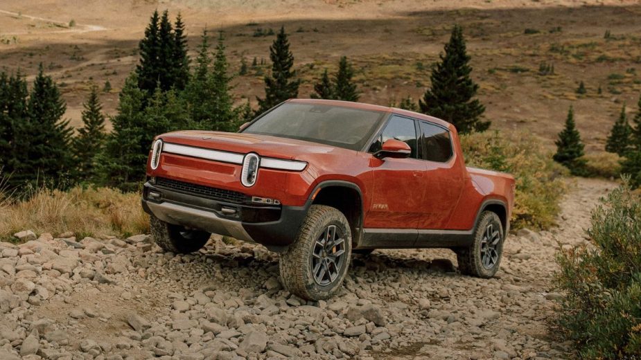 2023 Rivian R1T orange electric pickup truck driving up a hill