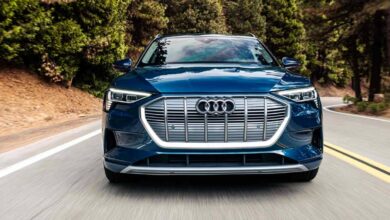 A blue 2023 Audi E-Tron is driving on the road.