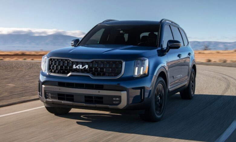 A blue 2023 Kia Telluride midsize SUV is driving on the road.