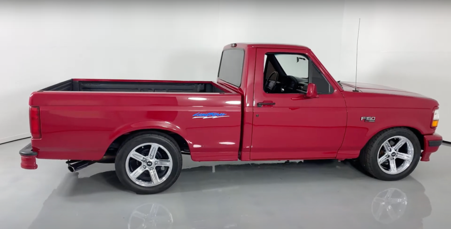 Side shot of a 1994 Red Ford F-150 SVT Lightning muscle truck parked in a showroom, white wall visible in the background.