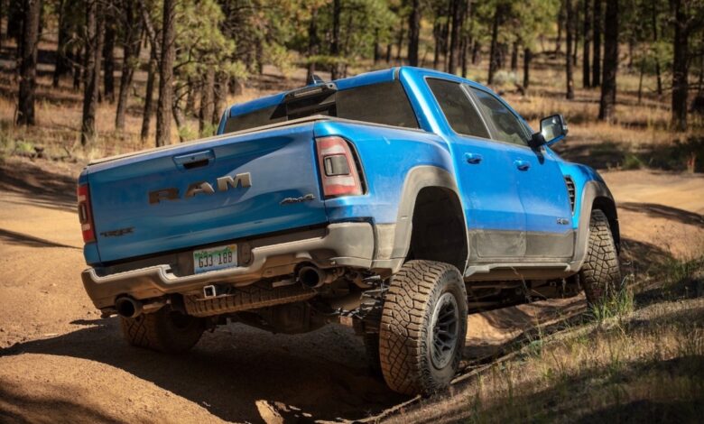 A blue Ram 1500 TRX parked on a dirt road, trees visible in the background.