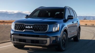 A blue Kia Telluride midsize SUV is driving on the road.