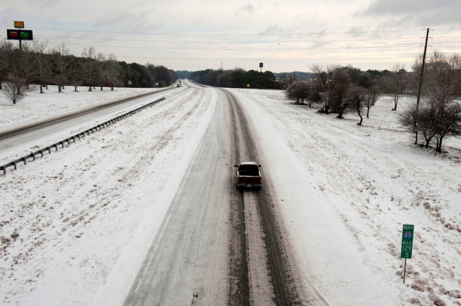A diesel truck is driving down a deserted and snowy highway on a cold winter day.