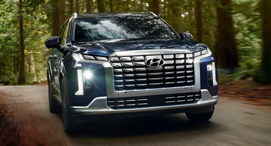 A blue 2023 Hyundai Palisade mid-size SUV is driving on the road. 