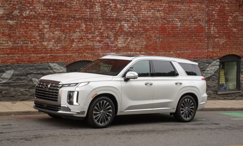 A white 2023 Hyundai Palisade midsize crossover SUV model parked on a street next to a red brick wall