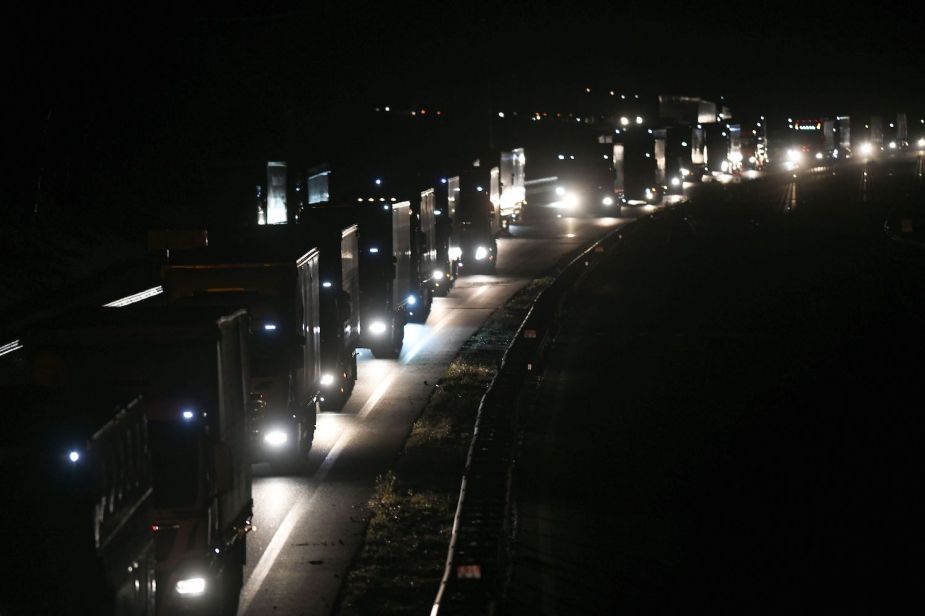 A row of semi-trucks are waiting in traffic on the interstate highway.