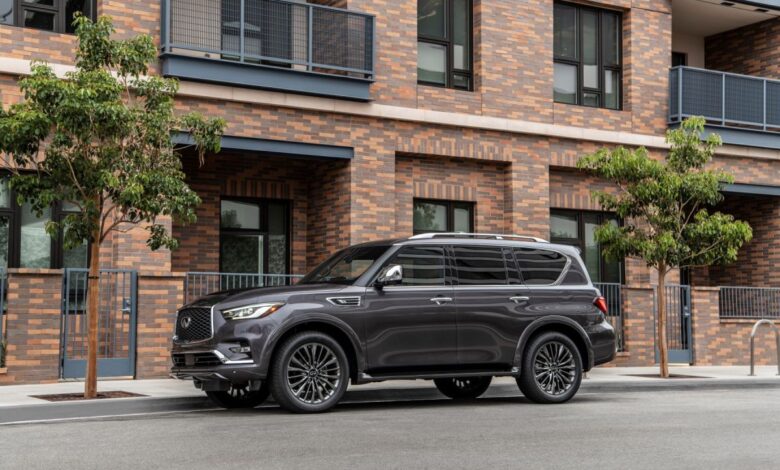 A dark gray 2023 Infiniti QX80 full-size luxury SUV model parked outside a brick apartment building
