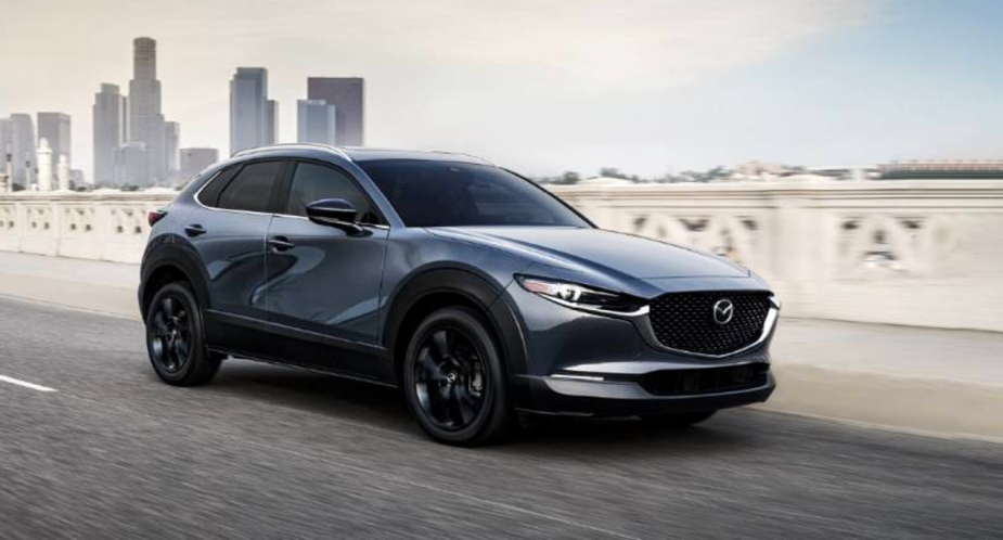 A gray 2023 Mazda CX-30 compact SUV is driving on the road. 