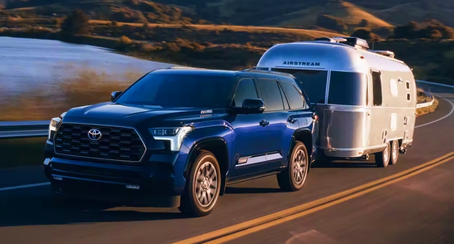 A blue 2023 Toyota Sequoia full-size SUV is pulling an Airstream trailer on the road. 