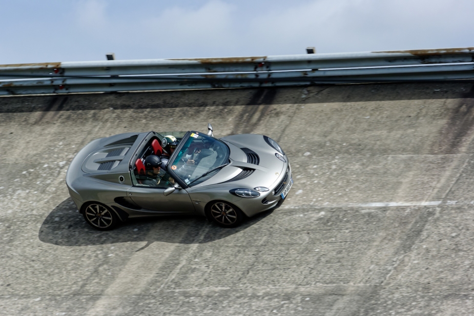A gray Lotus Elise convertible corners on the steep curves of the race track.