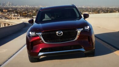A red 2024 Mazda CX-90 midsize SUV is driving on the road.