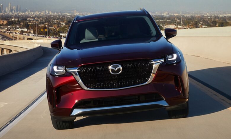 A red 2024 Mazda CX-90 midsize SUV is driving on the road.