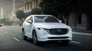 A white 2023 Mazda CX-5 small SUV is driving on the road.