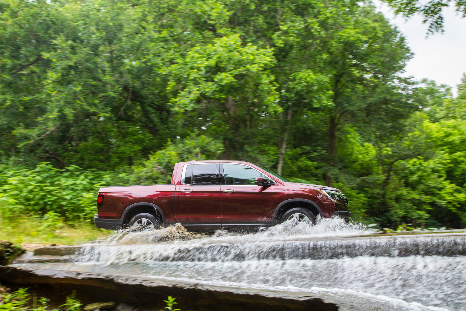 A Honda Ridgeline pickup truck fording a river, with trees visible in the background.