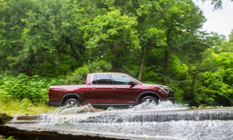 A Honda Ridgeline pickup truck fording a river, trees visible in the background.