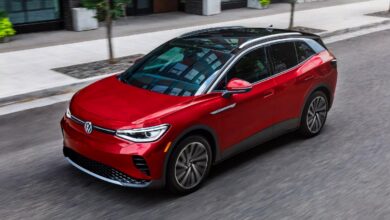 A red 2023 Volkswagen ID.4 small electric SUV is driving on the road.