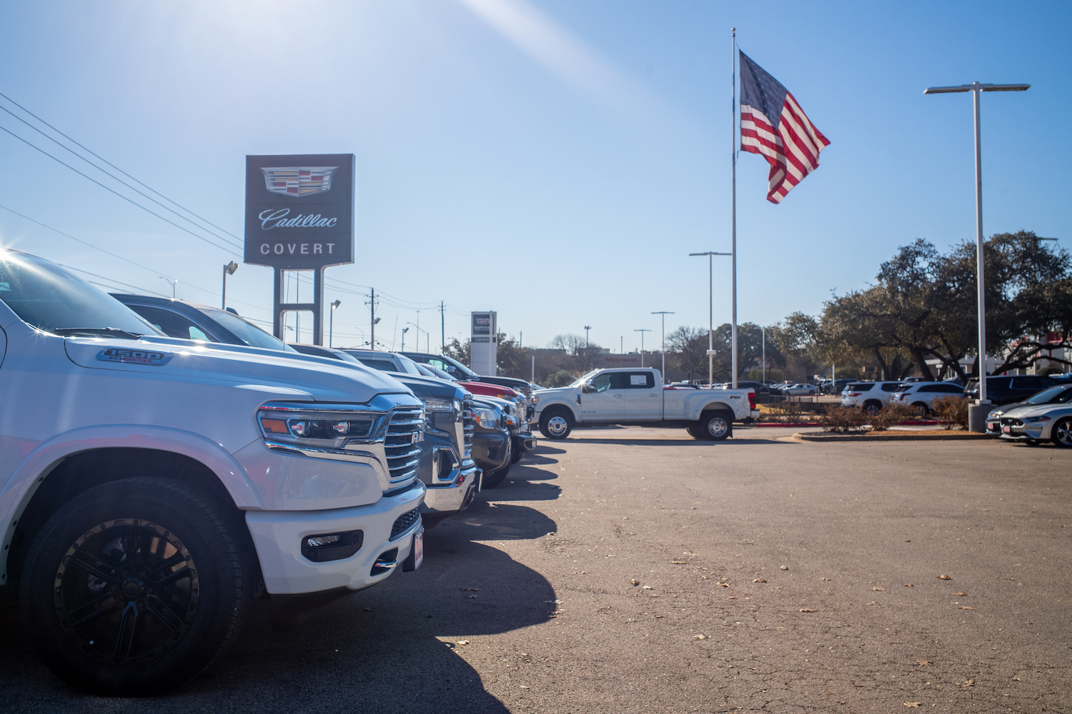 A row of different pickup trucks parked at a store, with the American flag in the background.