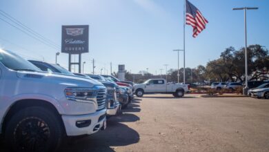 A row of various pickup trucks parked at a dealership, an American flag visible in the background.