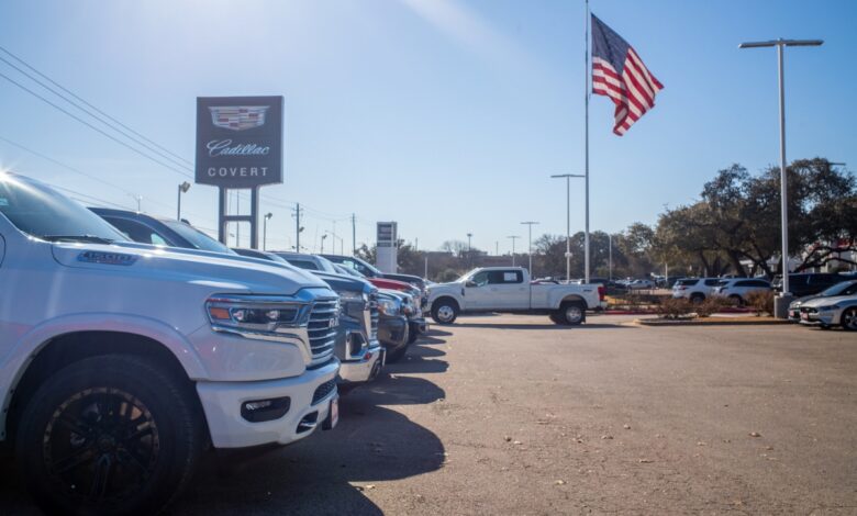 A row of various pickup trucks parked at a dealership, an American flag visible in the background.