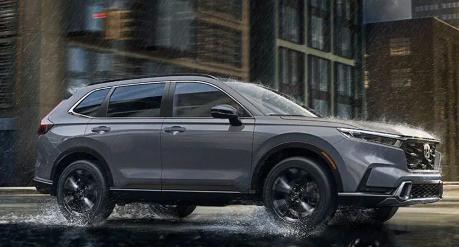 A small gray 2023 Honda CR-V SUV is driving on the road in the rain. 