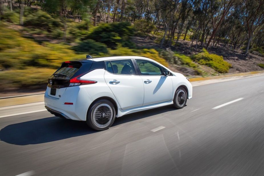 A white Nissan Leaf shows the proportions of its electric car while it is driving on a back road. 