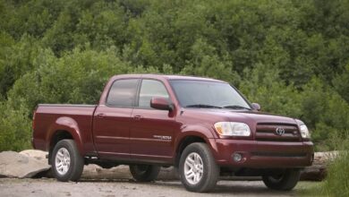 A maroon 2006 Toyota Tundra with a four-door cab parked on a dirt parking lot with green trees in the background.