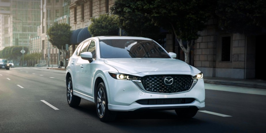 A small white 2023 Mazda CX-5 SUV is driving on the road. 