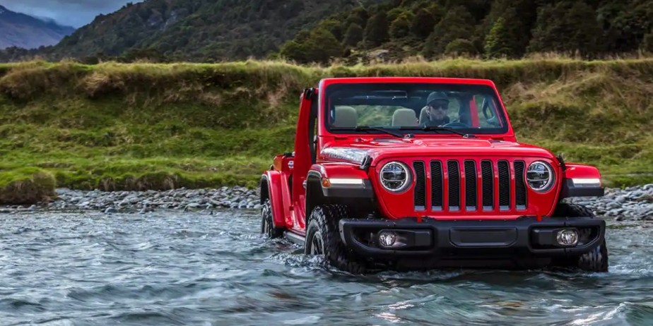 A small red Jeep Wrangler SUV is wading through the water. 