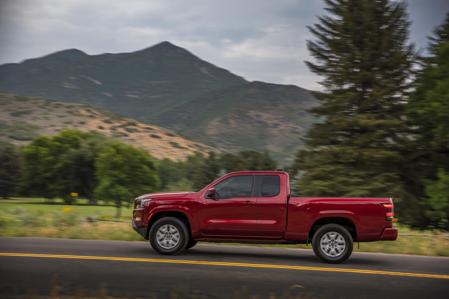 Side view of a red Nissan Titan mid-size pickup truck driving in front of a mountain range.