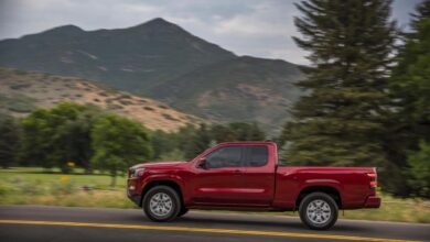 The profile view of a red midsize Nissan Titan pickup truck, driving in front of a mountain range.