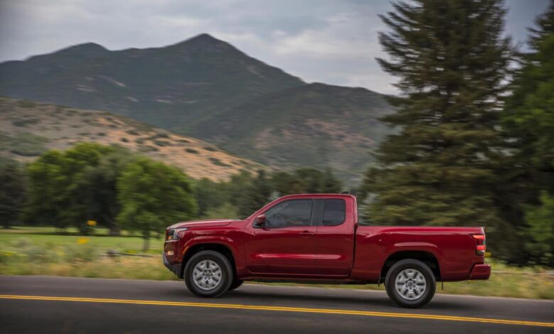 The profile view of a red midsize Nissan Titan pickup truck, driving in front of a mountain range.