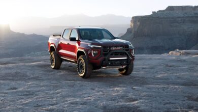 A red 2023 GMC Canyon AT4X Edition 1 midsize pickup truck model on top of a rocky cliff in the wilderness