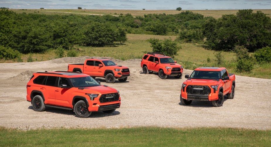 Four Toyota pickup trucks and SUVs parked together off-road, all painted the same orange.