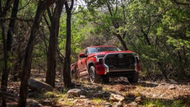 A red Toyota Tundra pickup truck shows off its off-road capability as it navigates a trail through the woods.