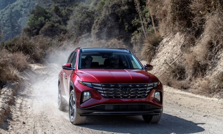 A red 2023 Hyundai Tucson compact SUV model driving on a dirt road as its tires kick up dust