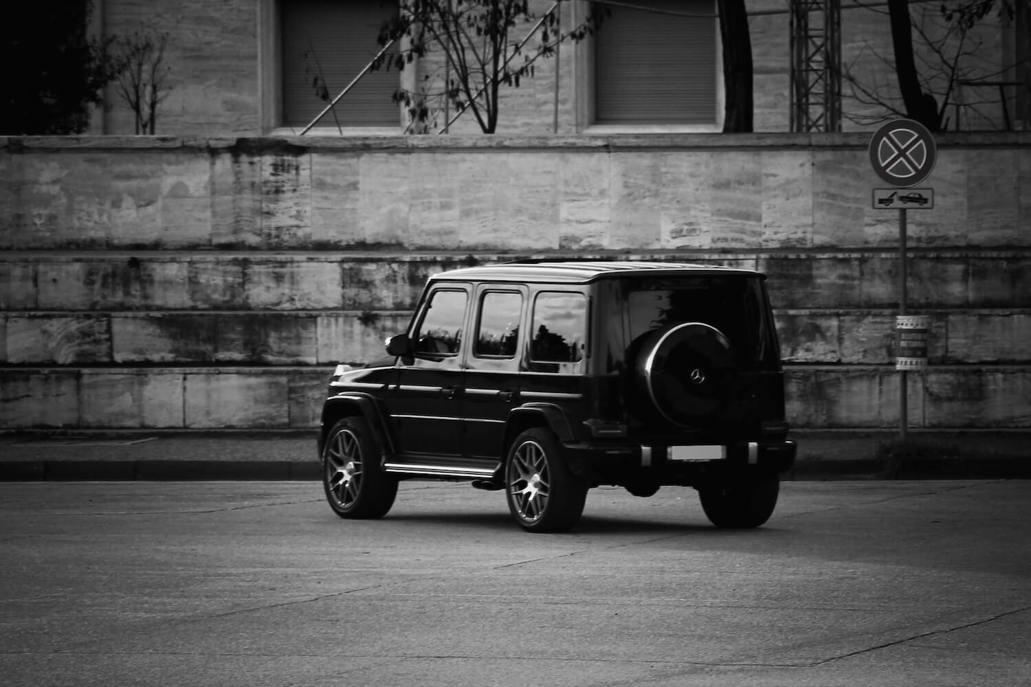 Black and white photo of a Mercedes Wagon G-Class SUV parked facing the camera, a brick wall visible in the background.